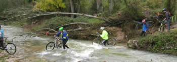 ciclistas atravessando rio com gua pelos joelhos e levando as bicicletas  mo
